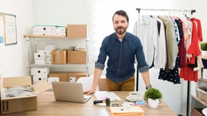 joven-empresario-hispano-detras-su-escritorio-oficina-trabajando-hacer-paquetes-ropa-moda-enviar-sus-clientes-edit